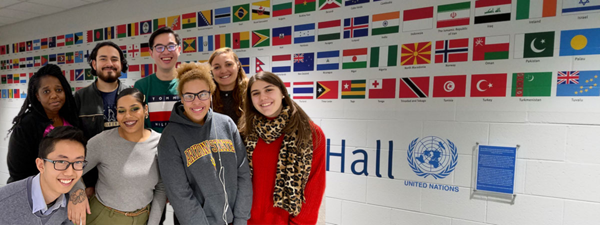 Group of international students standing in front of CLC's Global Community Wall