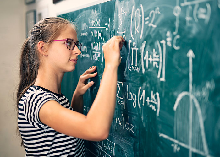 Young female student solving math problem on blackboard
