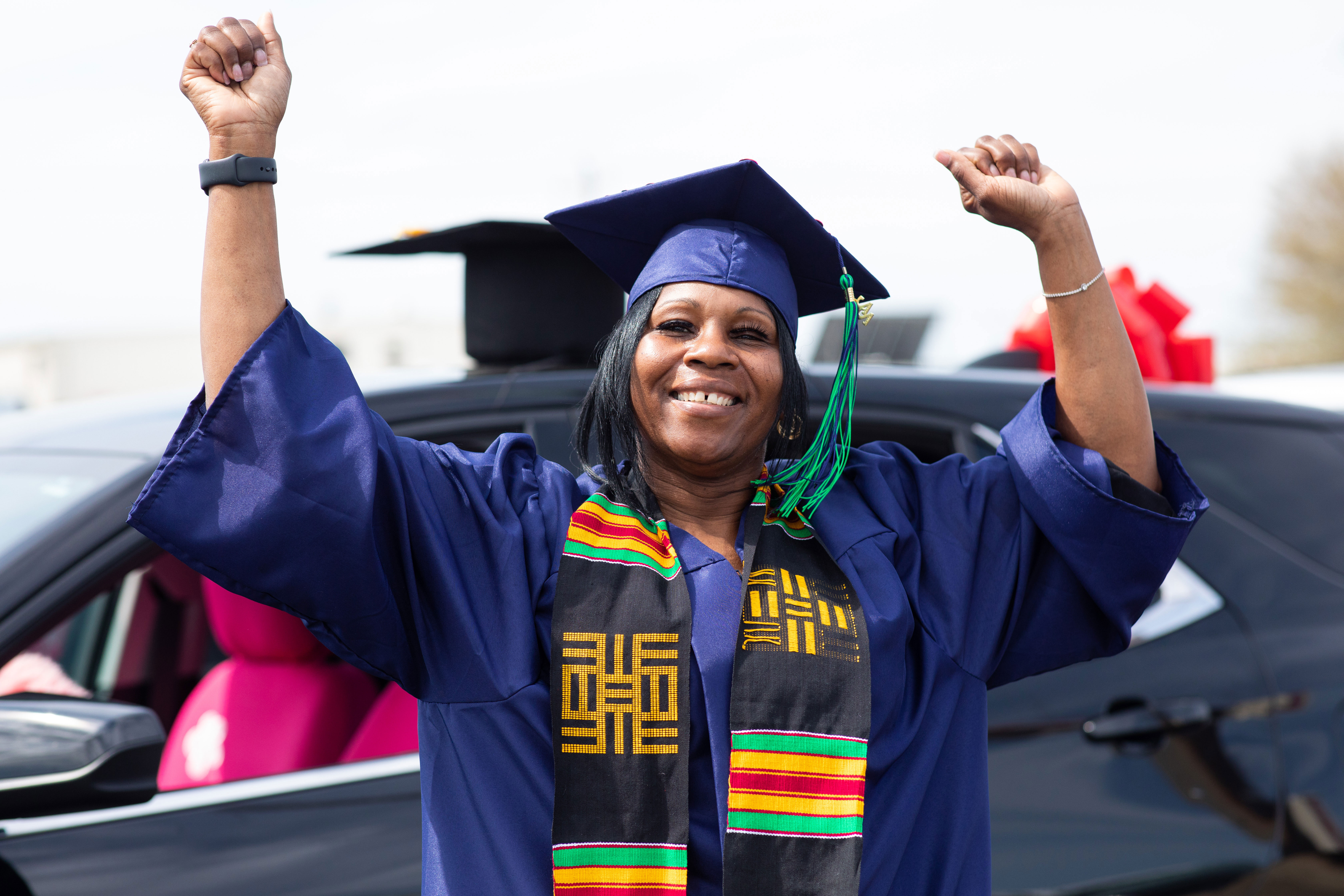 Female black CLC graduate raising her hands to celebrate
