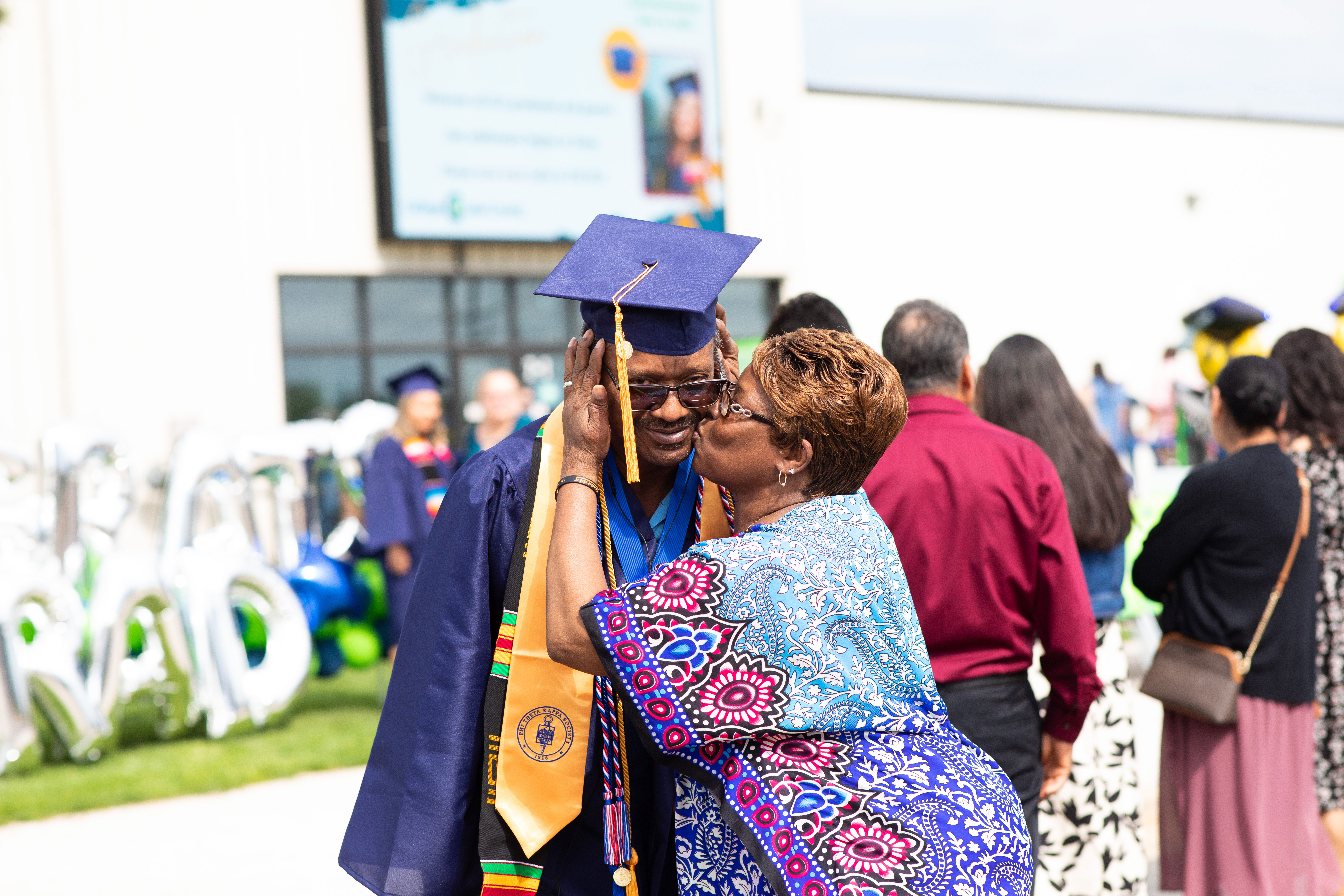 Male black graduate getting a kiss on the cheek from female family member