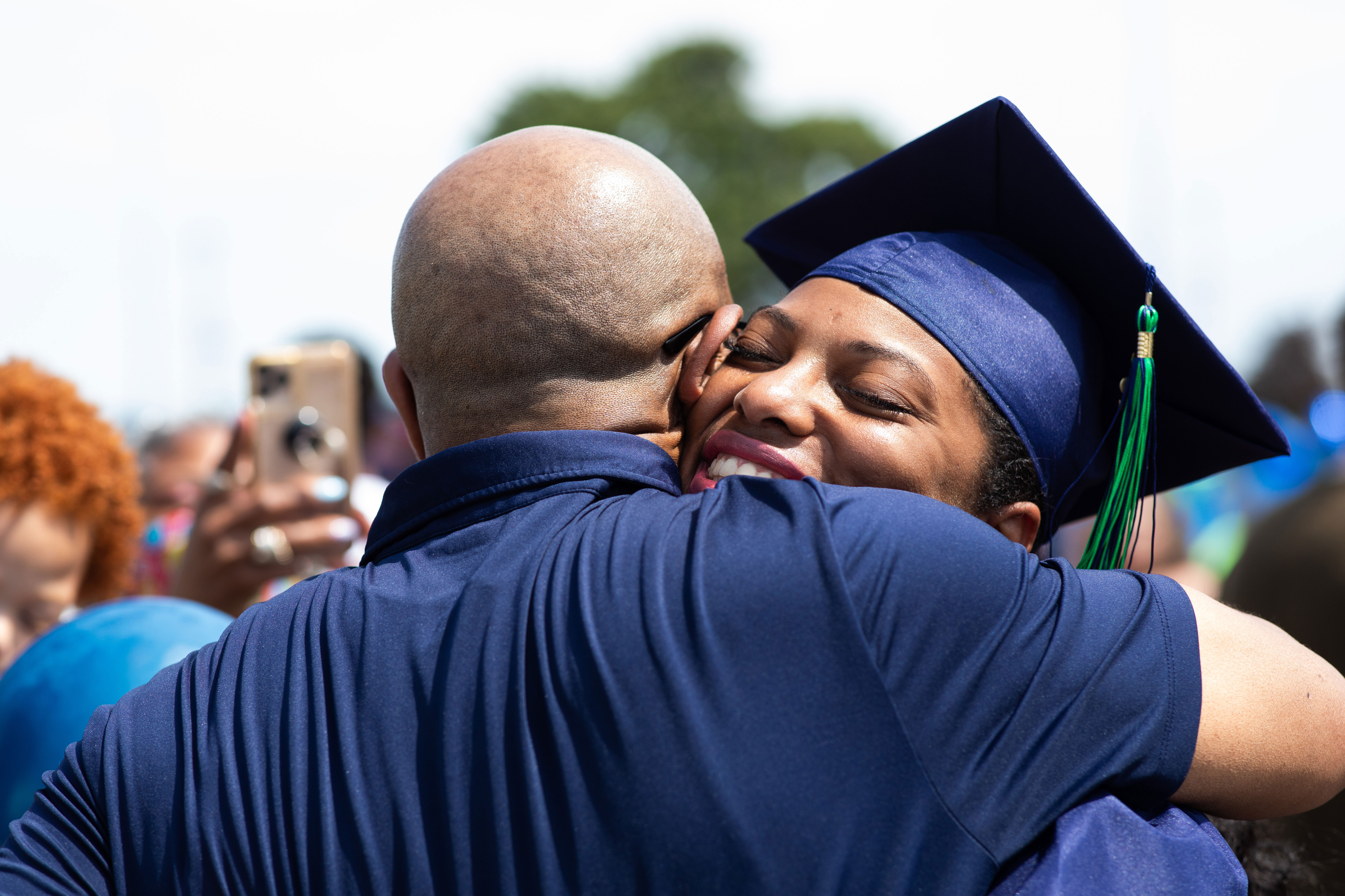 Female black graduate embracing family member